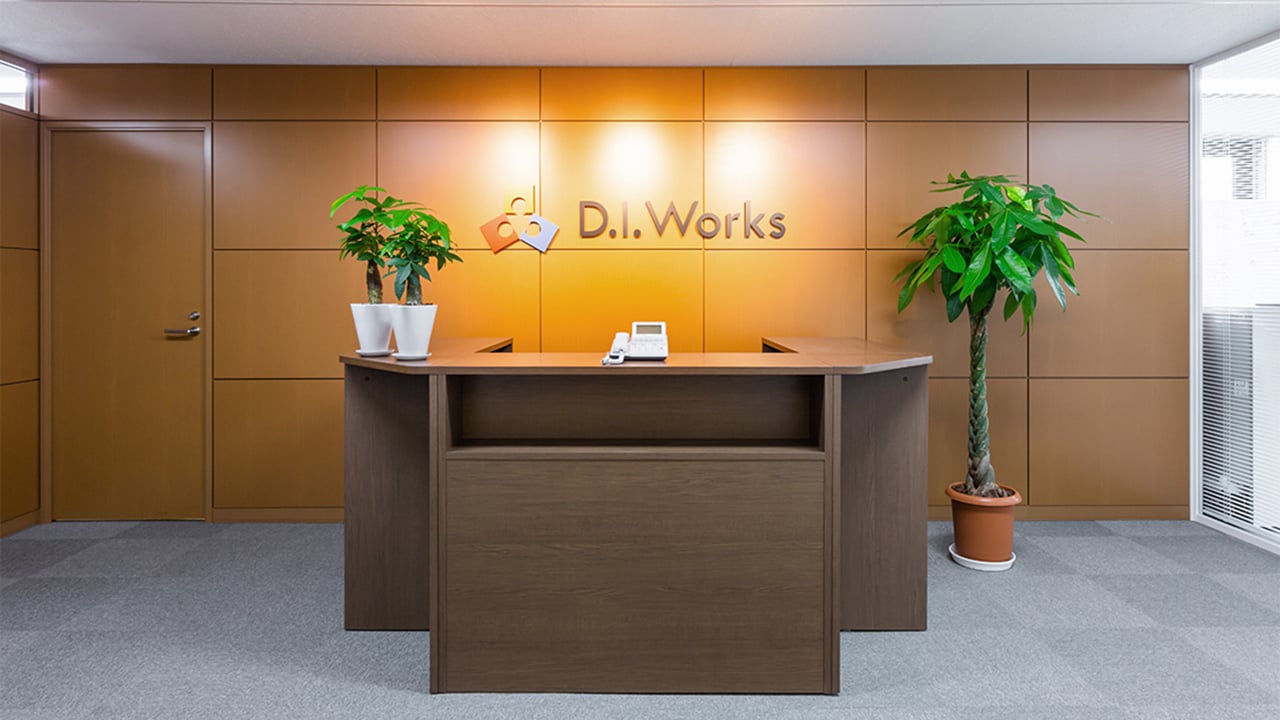 株式会社D.I.Works様のオフィスエントランス。木目調の受付カウンターと観葉植物を配置した空間